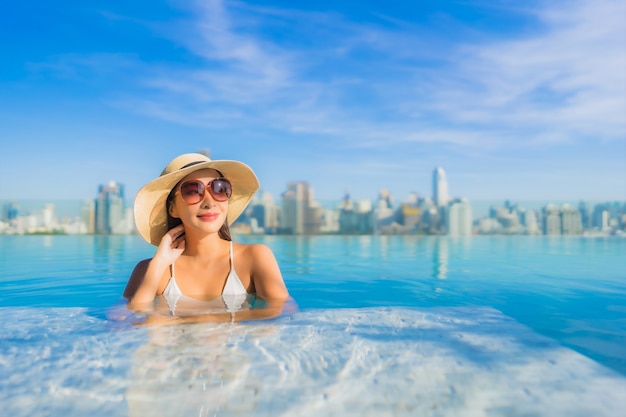 Free photo portrait beautiful young asian woman relaxing around outdoor swimming pool with city view