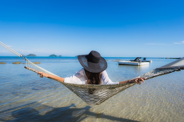 Free photo portrait beautiful young asian woman sitting on hammock around sea beach ocean for relax