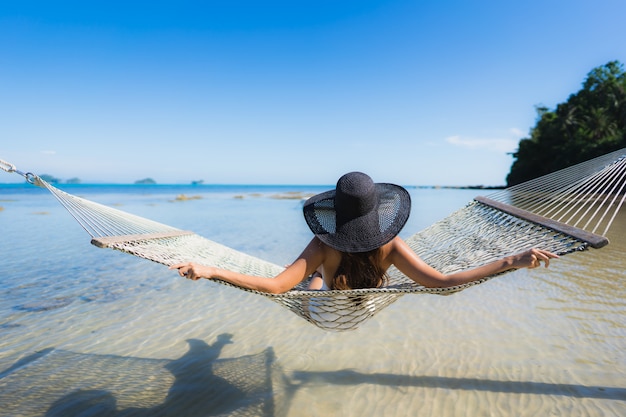 Free photo portrait beautiful young asian woman sitting on hammock around sea beach ocean for relax