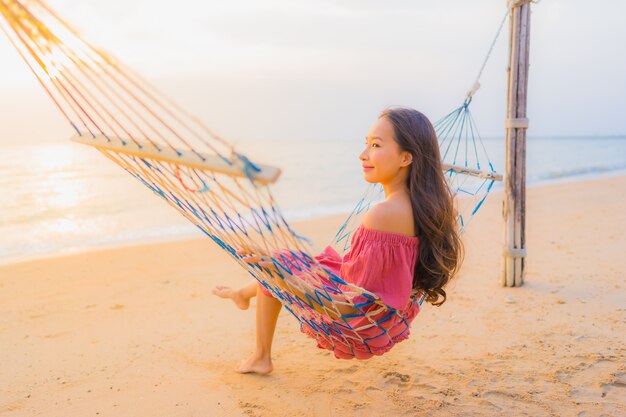 Portrait beautiful young asian woman sitting on the hammock with smile happy neary beach sea and oce