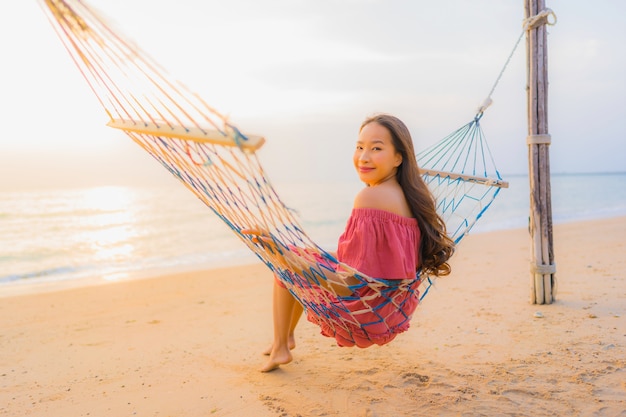 Portrait beautiful young asian woman sitting on the hammock with smile happy neary beach sea and oce