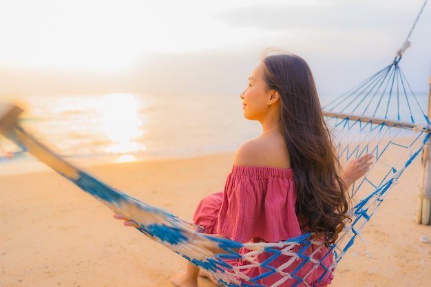 Free photo portrait beautiful young asian woman sitting on the hammock with smile happy neary beach sea and oce