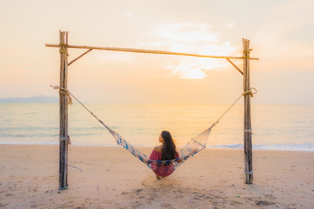 Free Photo portrait beautiful young asian woman sitting on the hammock with smile happy neary beach sea and oce