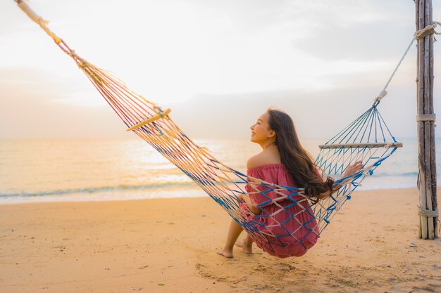 Portrait beautiful young asian woman sitting on the hammock with smile happy neary beach sea and oce