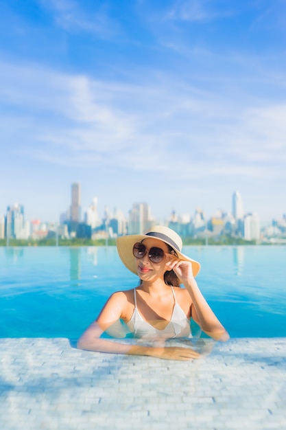 Free photo portrait beautiful young asian woman smile relax leisure around outdoor swimming pool with city view