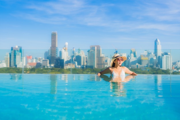 Free photo portrait beautiful young asian woman smile relax leisure around outdoor swimming pool with city view