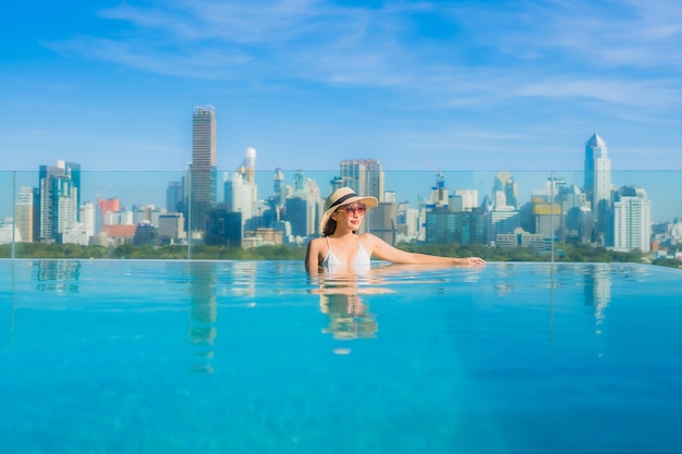 Free photo portrait beautiful young asian woman smile relax leisure around outdoor swimming pool with city view