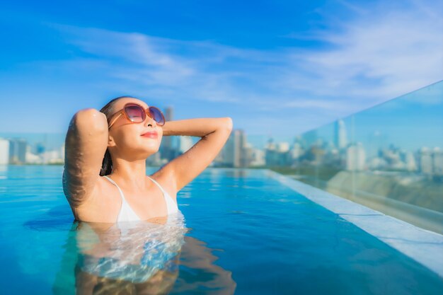 Free photo portrait beautiful young asian woman smile relax leisure around outdoor swimming pool with city view