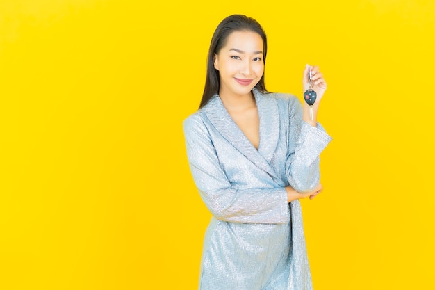 Portrait beautiful young asian woman smile with car key on yellow wall