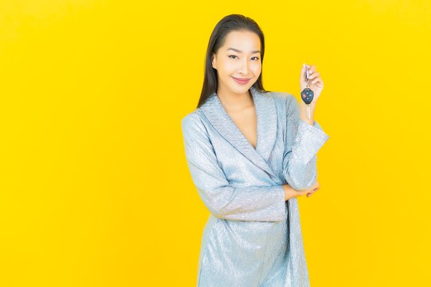 Portrait beautiful young asian woman smile with car key on yellow wall