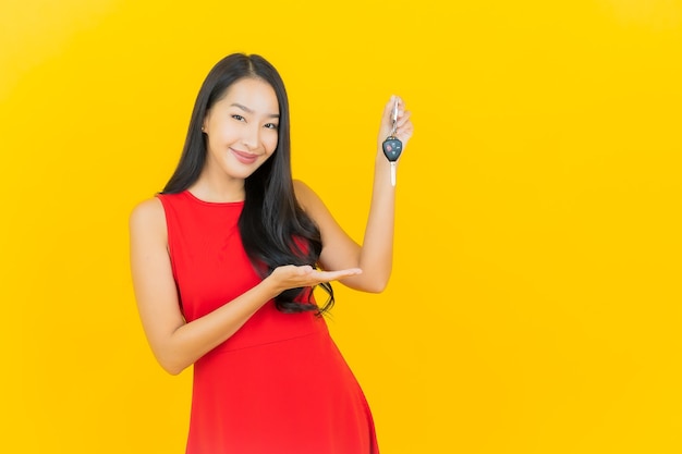 Free photo portrait beautiful young asian woman smile with car key on yellow wall