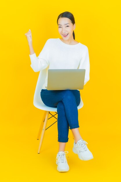 Portrait beautiful young asian woman smile with computer laptop on yellow