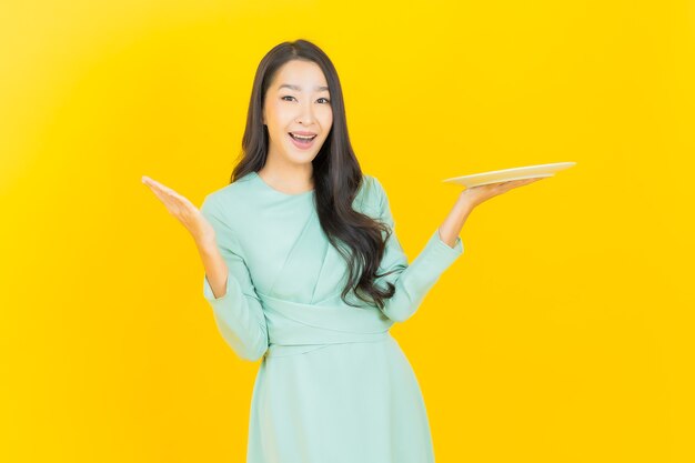 Free Photo portrait beautiful young asian woman smile with empty plate dish on yellow