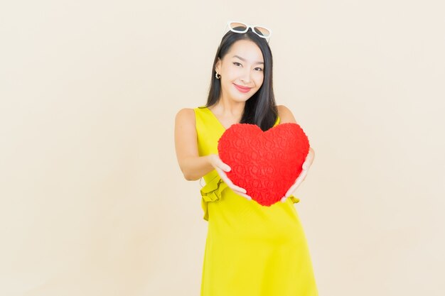 Portrait beautiful young asian woman smile with heart pillow shape on color wall