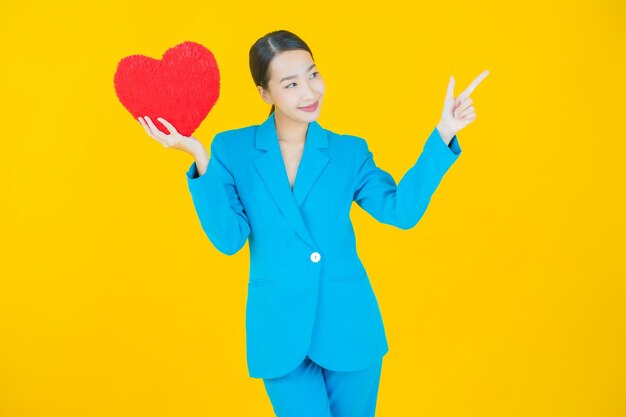 Portrait beautiful young asian woman smile with heart pillow shape on yellow