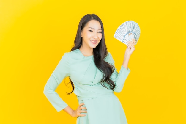 Portrait beautiful young asian woman smile with a lot of cash and money on yellow