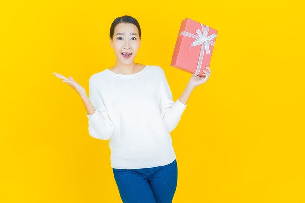 Portrait beautiful young asian woman smile with red gift box on yellow