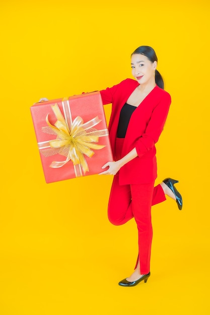 Portrait beautiful young asian woman smile with red gift box on yellow