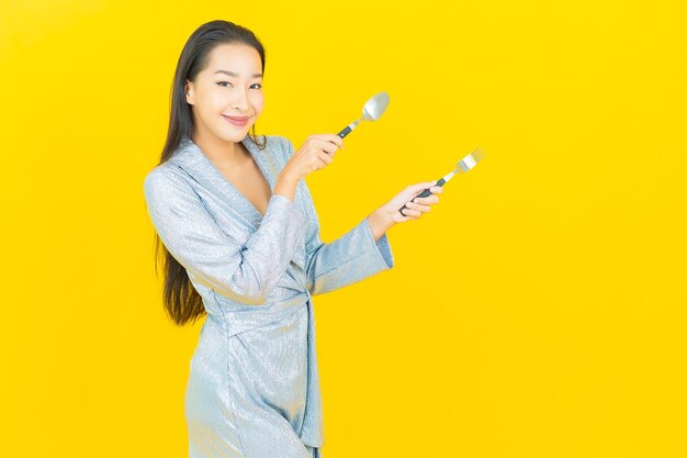 Portrait beautiful young asian woman smile with spoon and fork on yellow wall