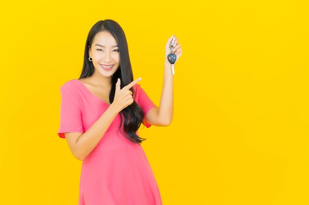 Portrait beautiful young asian woman smiles with car key on yellow wall