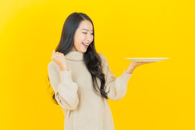 Portrait beautiful young asian woman smiles with empty plate dish on yellow wall