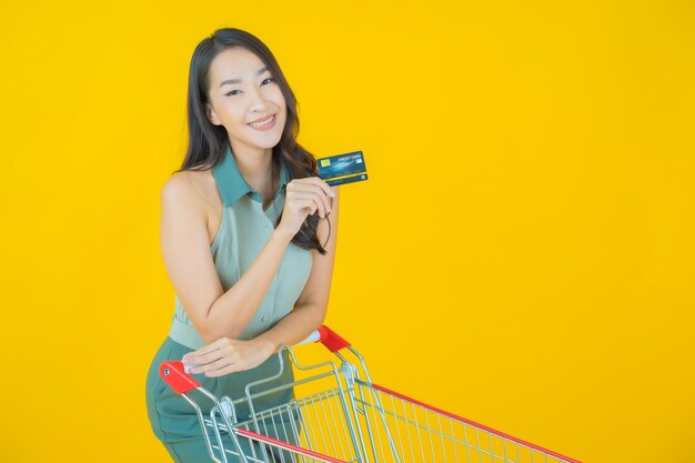 Portrait of beautiful young asian woman smiles with grocery basket from supermarket on yellow wall