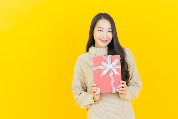 Portrait beautiful young asian woman smiles with red gift box on yellow wall