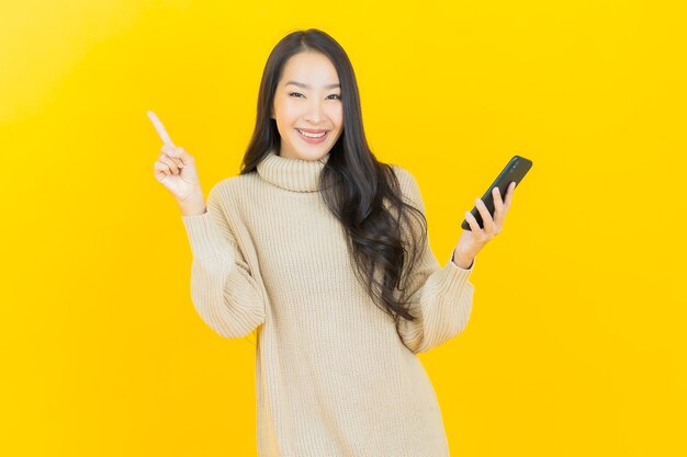 Portrait beautiful young asian woman smiles with smart mobile phone on yellow wall