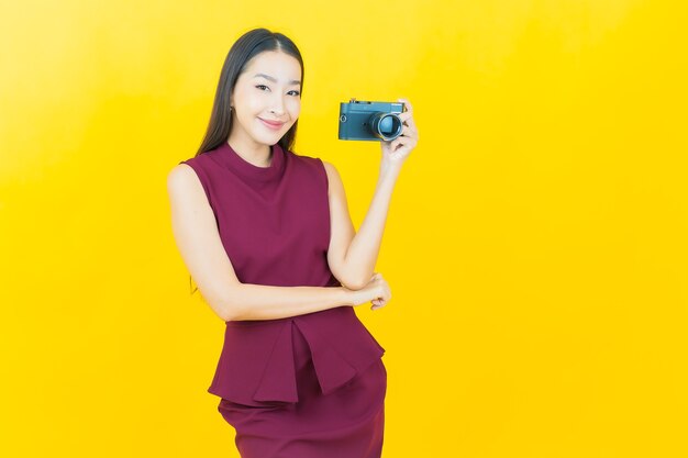 Portrait beautiful young asian woman use camera on yellow wall