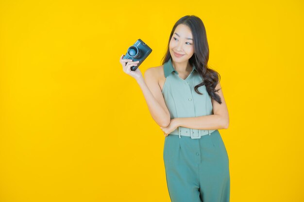 Portrait of beautiful young asian woman use camera on yellow wall