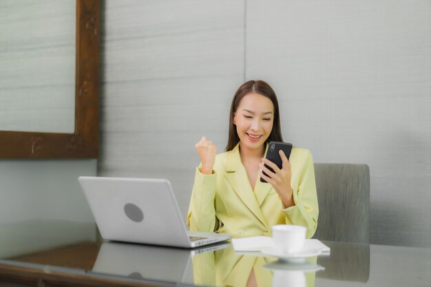 Portrait beautiful young asian woman use computer laptop with smart mobile phone on working table at interior room