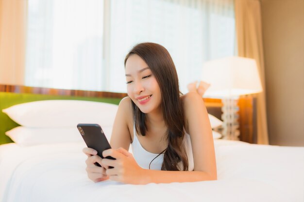 Portrait beautiful young asian woman use smart mobile phone on bed in bedroom interior