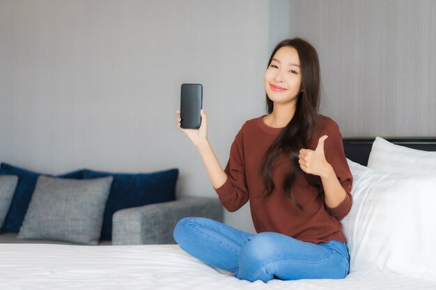 Portrait beautiful young asian woman use smart mobile phone on bed in bedroom interior