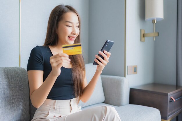 Portrait beautiful young asian woman use smart mobile phone or laptop with credit card on sofa in living room area