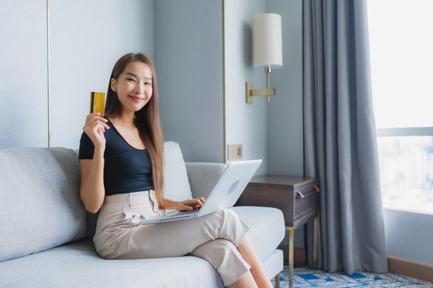 Portrait beautiful young asian woman use smart mobile phone or laptop with credit card on sofa in living room area