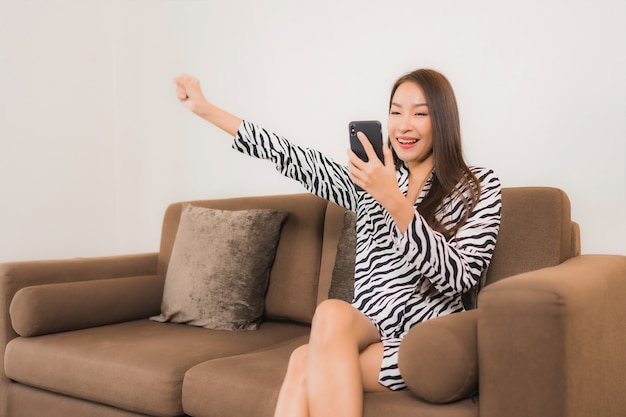 Portrait beautiful young asian woman use smart mobile phone on sofa in living room interior