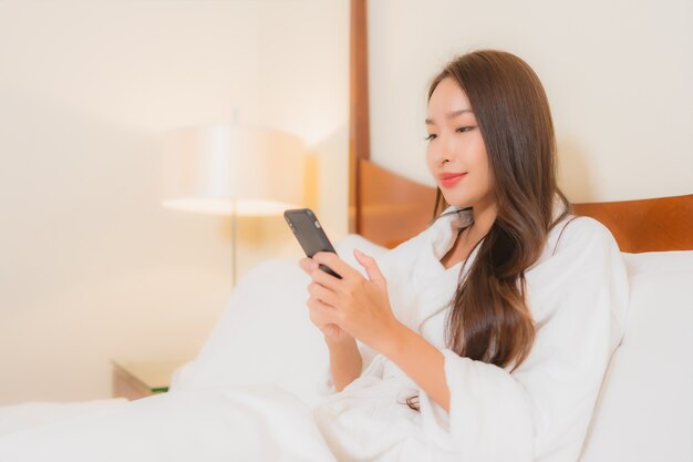 Portrait beautiful young asian woman using smart mobile phone on bed in bedroom interior