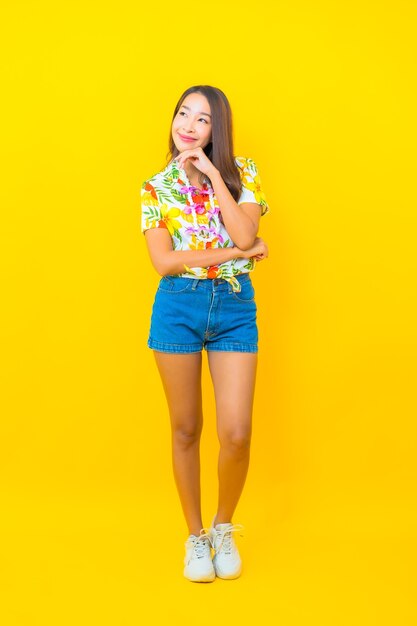 Portrait of beautiful young asian woman wearing colorful shirt on yellow wall