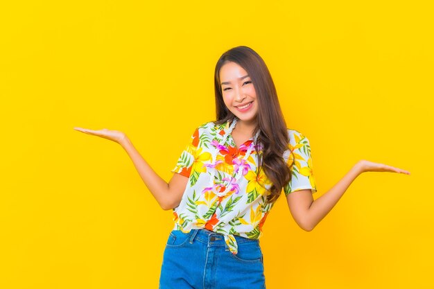 Portrait of beautiful young asian woman wearing colorful shirt on yellow wall