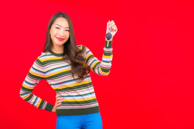 Portrait beautiful young asian woman with car key on red isolated wall