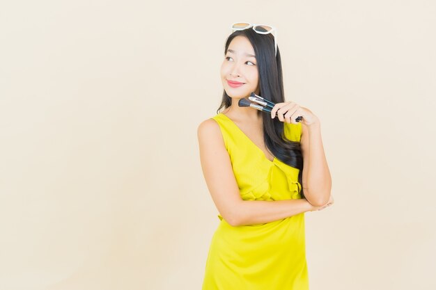 Portrait beautiful young asian woman with cosmeti make up brush on color wall