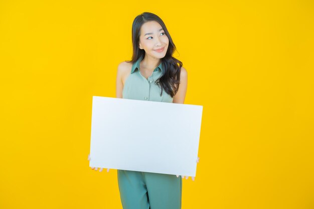 Portrait of beautiful young asian woman with empty white billboard on yellow wall