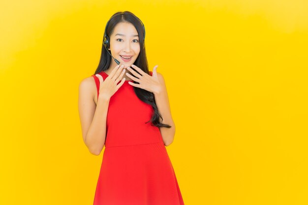 Portrait beautiful young asian woman with headset for communication and support call center service on yellow wall