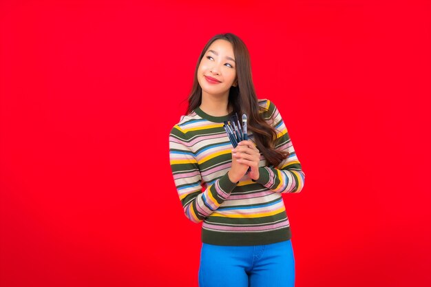 Portrait beautiful young asian woman with make up brush and cosmetic on red wall