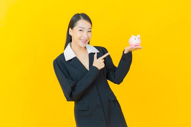 Portrait beautiful young asian woman with piggy bank on color wall