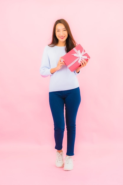 Portrait beautiful young asian woman with red gift box on pink isolated wall