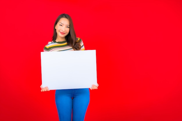 Free Photo portrait beautiful young asian woman with white empty billboard on red wall