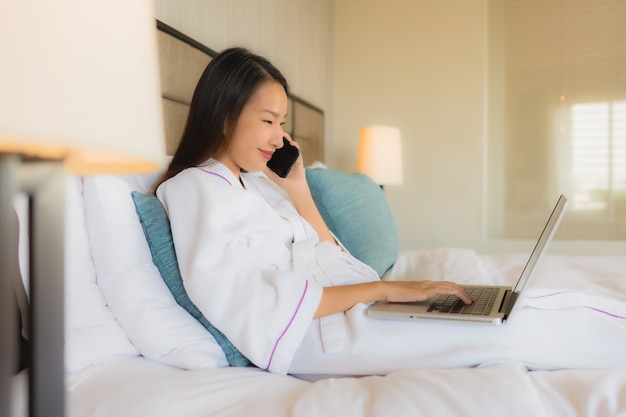 Portrait beautiful young asian women using laptop or computer with mobile on bed