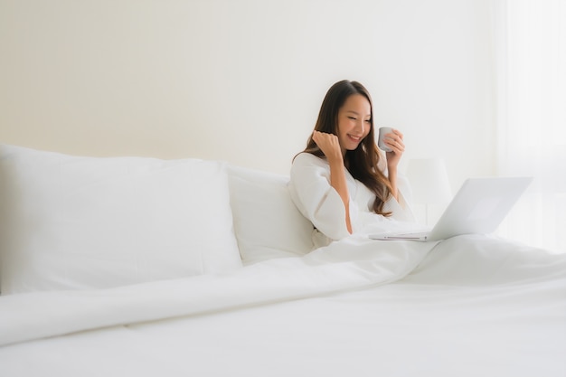 Portrait beautiful young asian women with coffee cup and computer laptop on bed