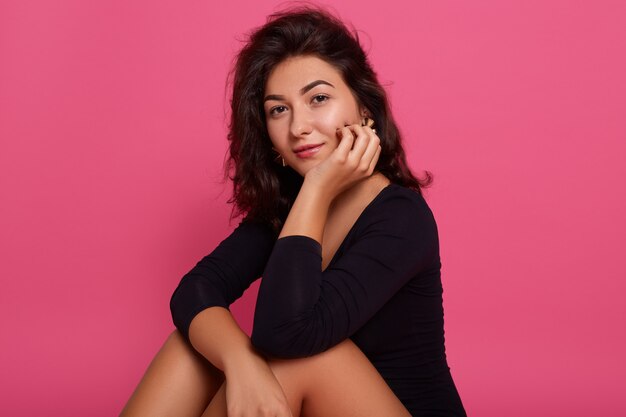 Portrait beautiful young caucasian woman wearing black shirt, sitting on floor with hands under chin